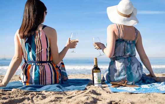 Women drinking Kris Pinot Gris wine on the beach